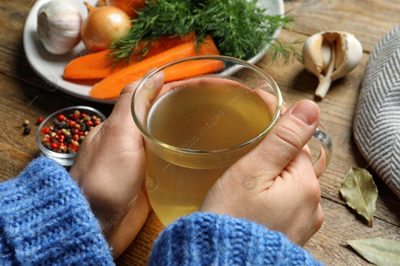 Photo of Woman with glass cup of hot delicious bouillon at wooden table, closeup