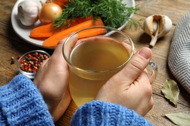 Woman with glass cup of hot delicious bouillon at wooden table, closeup