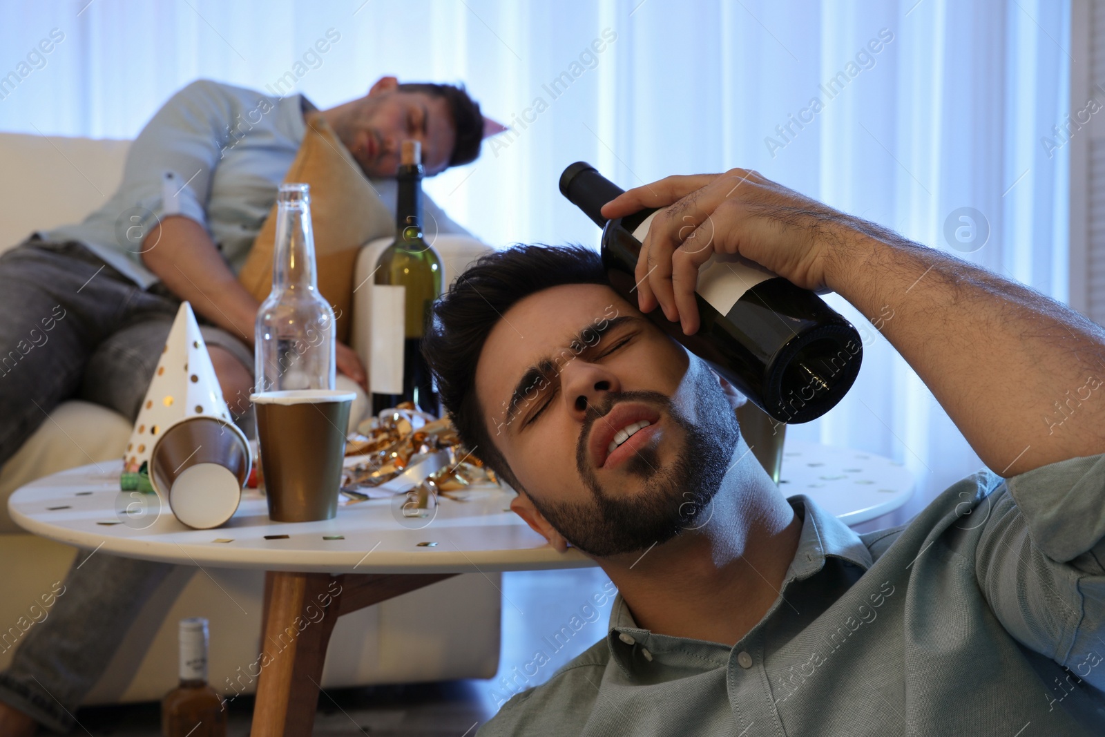 Photo of Young man suffering from hangover in messy room after party