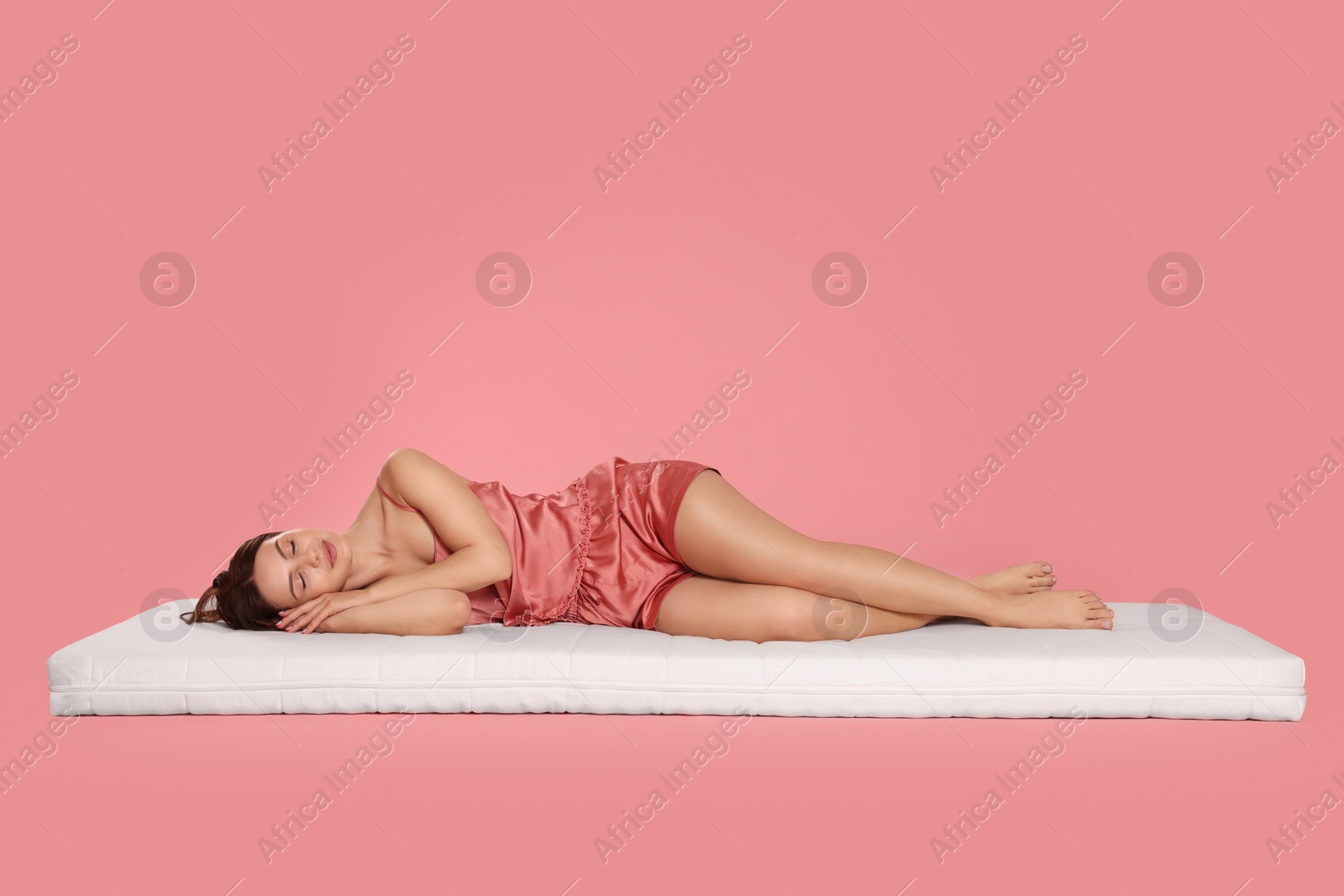 Photo of Young woman sleeping on soft mattress against pale pink background