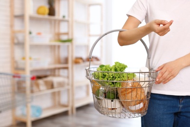 Photo of Woman with shopping basket full of products in grocery store, closeup