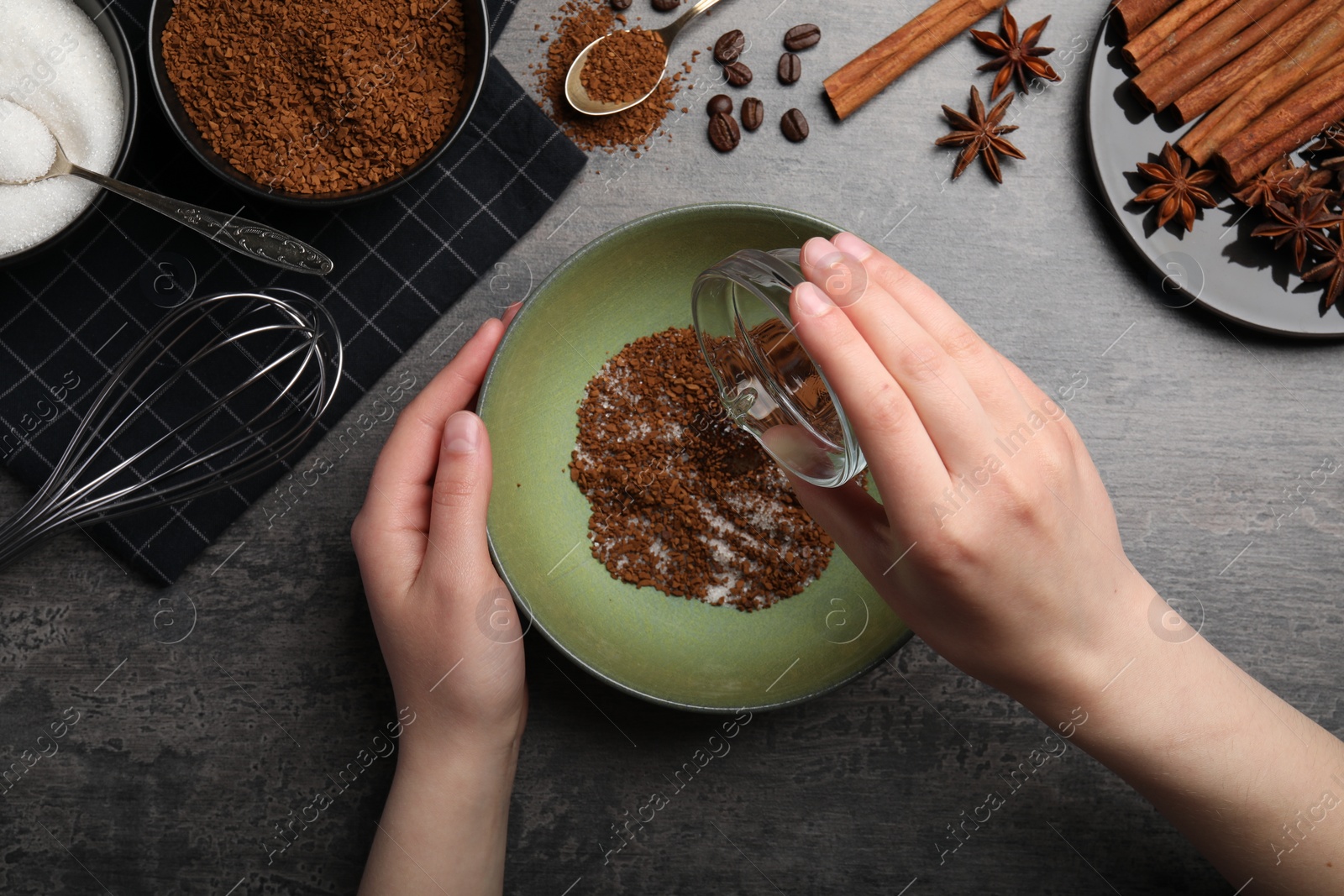 Photo of Making dalgona coffee. Woman pouring water into bowl at gray table, top view