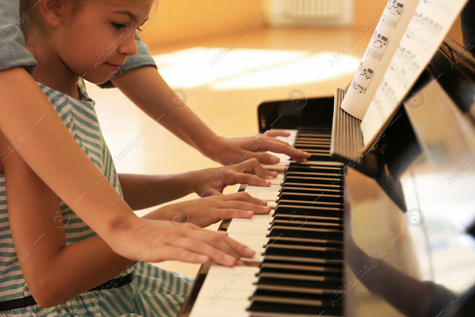 Photo of Young woman teaching little girl to play piano indoors