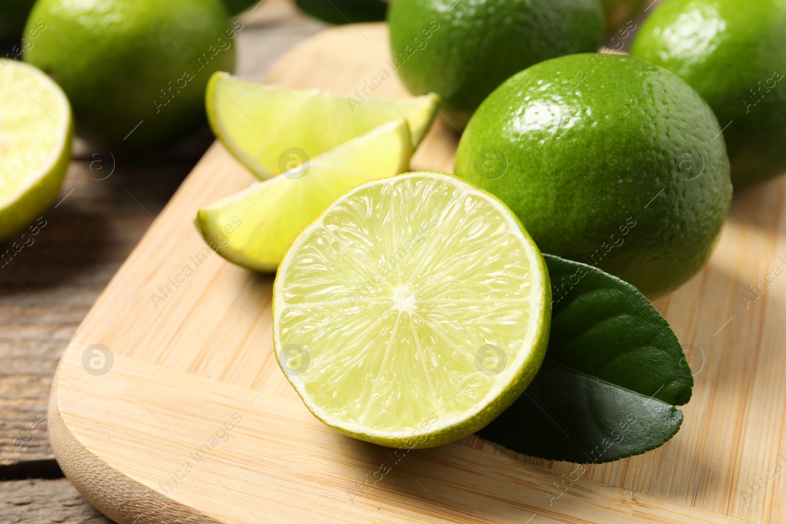 Photo of Whole and cut fresh limes on wooden table, closeup