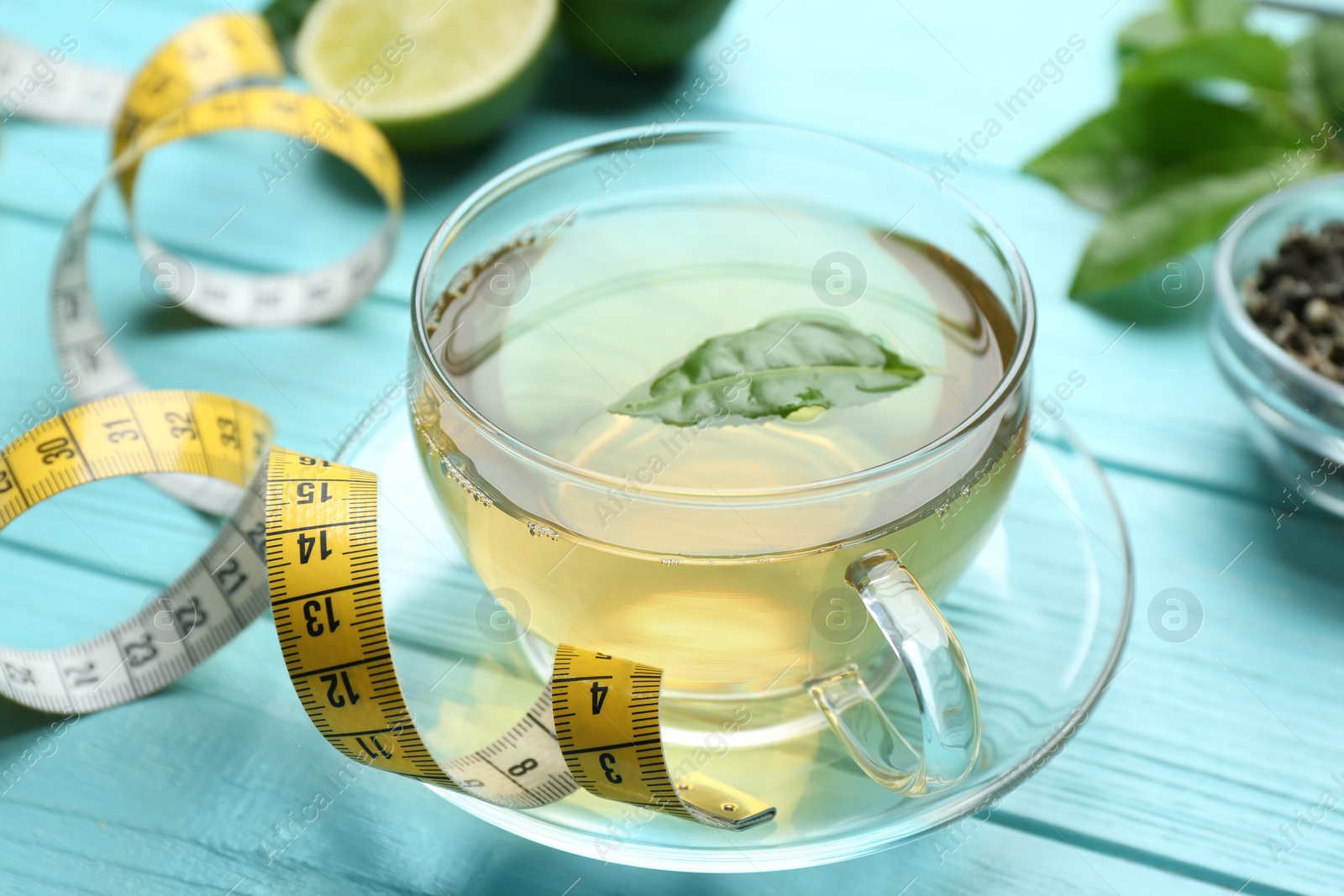 Photo of Cup of herbal diet tea and measuring tape on light blue wooden table