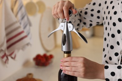 Photo of Romantic dinner. Woman opening wine bottle with corkscrew in kitchen, closeup