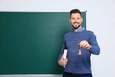 Photo of Teacher with school bell near chalkboard indoors. Space for text