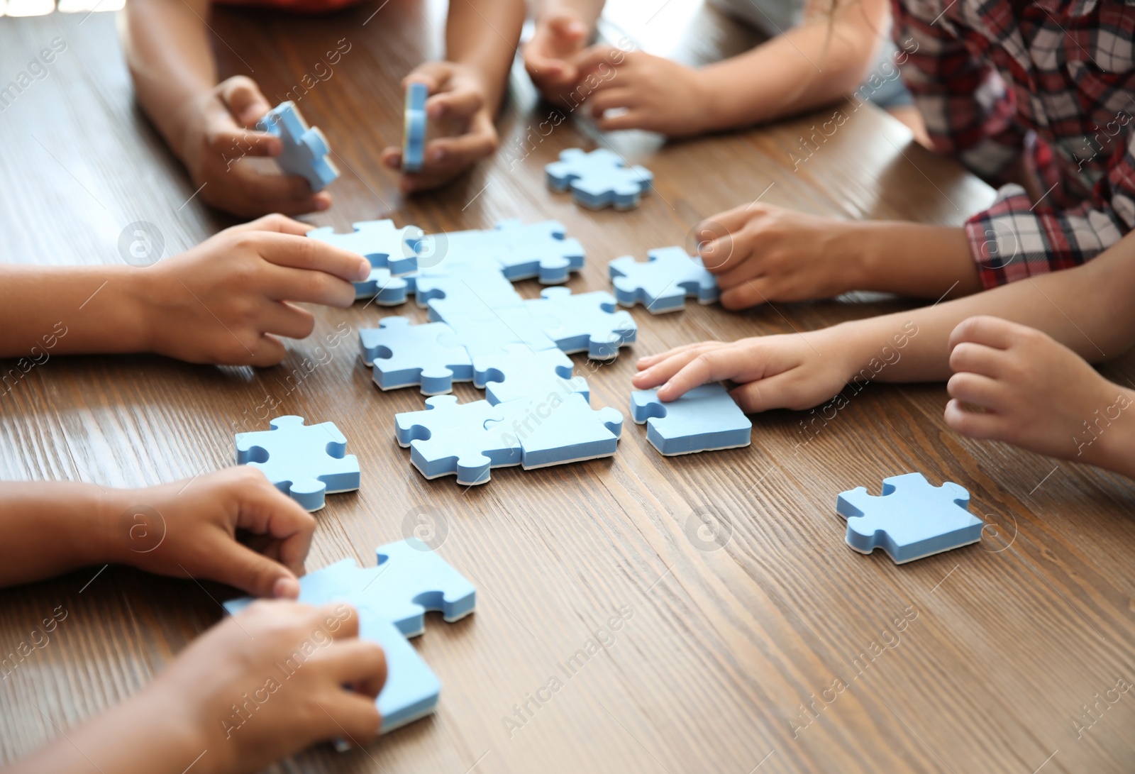 Photo of Little children playing with puzzle at table, focus on hands. Unity concept