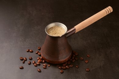 Photo of Turkish coffee in cezve and beans on dark table