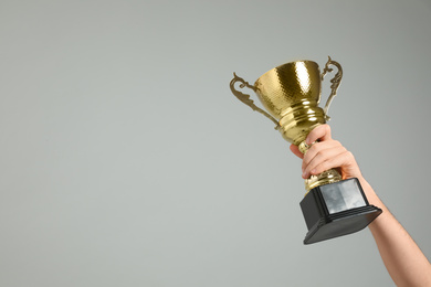 Man holding gold trophy cup on light grey background, closeup. Space for text
