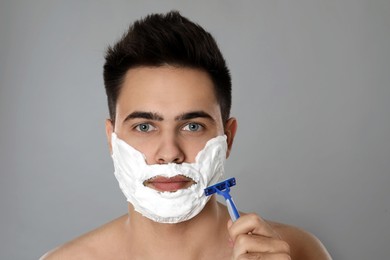 Photo of Handsome young man shaving with razor on grey background