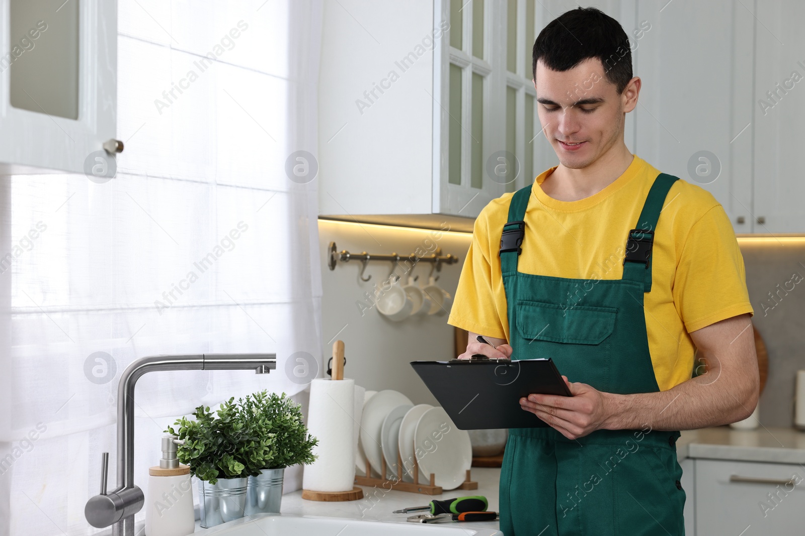 Photo of Smiling plumber with clipboard near faucet in kitchen