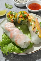 Plate with tasty spring rolls on grey textured table, closeup