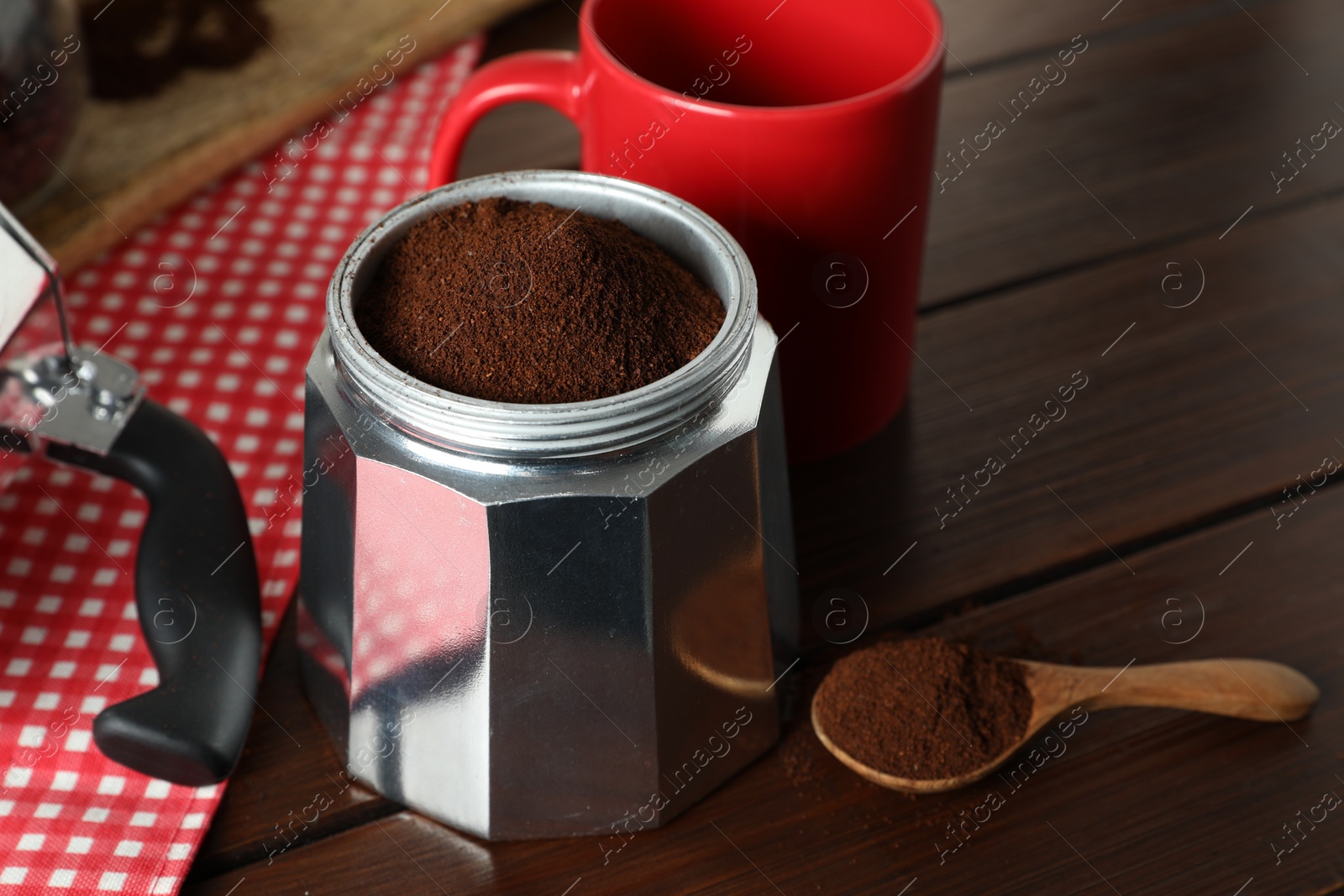 Photo of Moka pot with ground coffee and spoon on wooden table, closeup