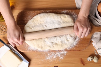 Woman rolling dough with wooden pin at table, top view