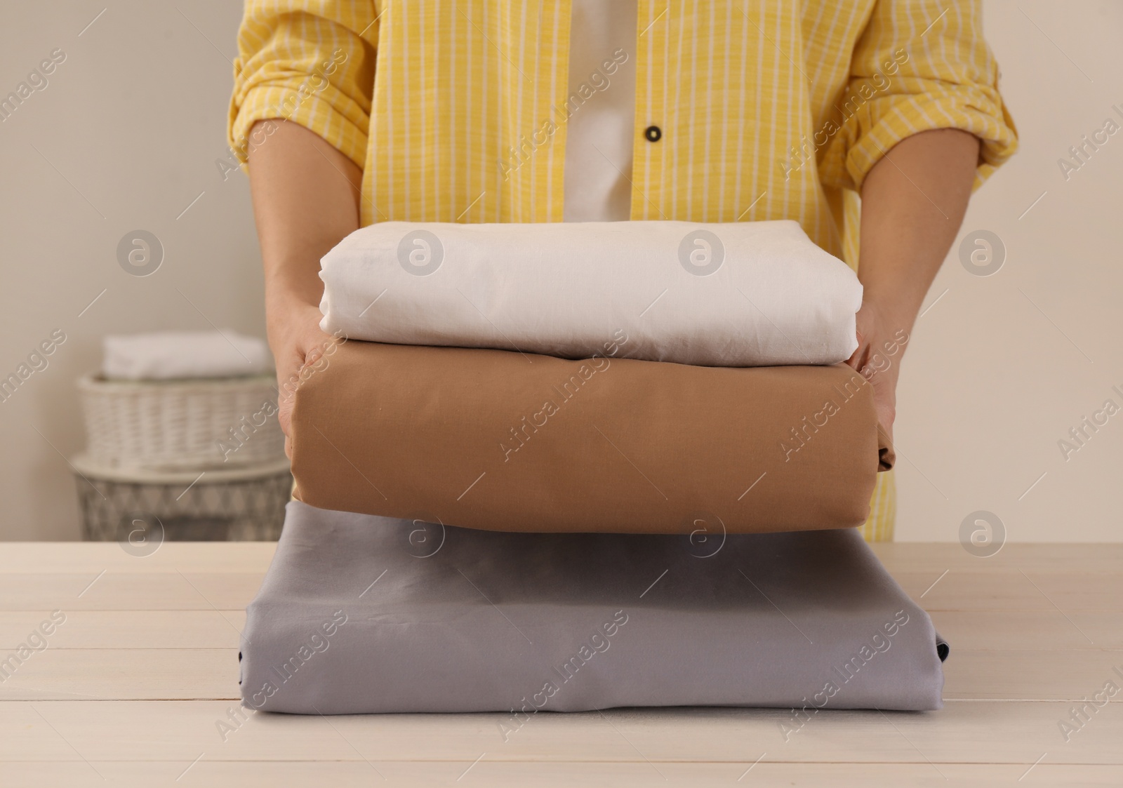 Photo of Woman with clean bed linens at white wooden table in laundry room, closeup