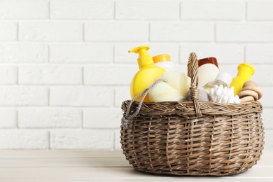 Photo of Wicker basket full of different baby cosmetic products, accessories and toy on white wooden table. Space for text