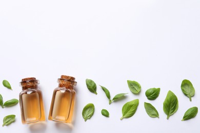 Photo of Bottles of essential basil oil and fresh leaves on white background, flat lay. Space for text