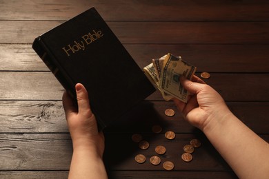 Photo of Donate and give concept. Woman with dollar banknotes, coins and Bible at wooden table, closeup