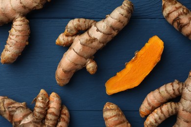 Photo of Whole and cut turmeric roots on blue wooden table, flat lay