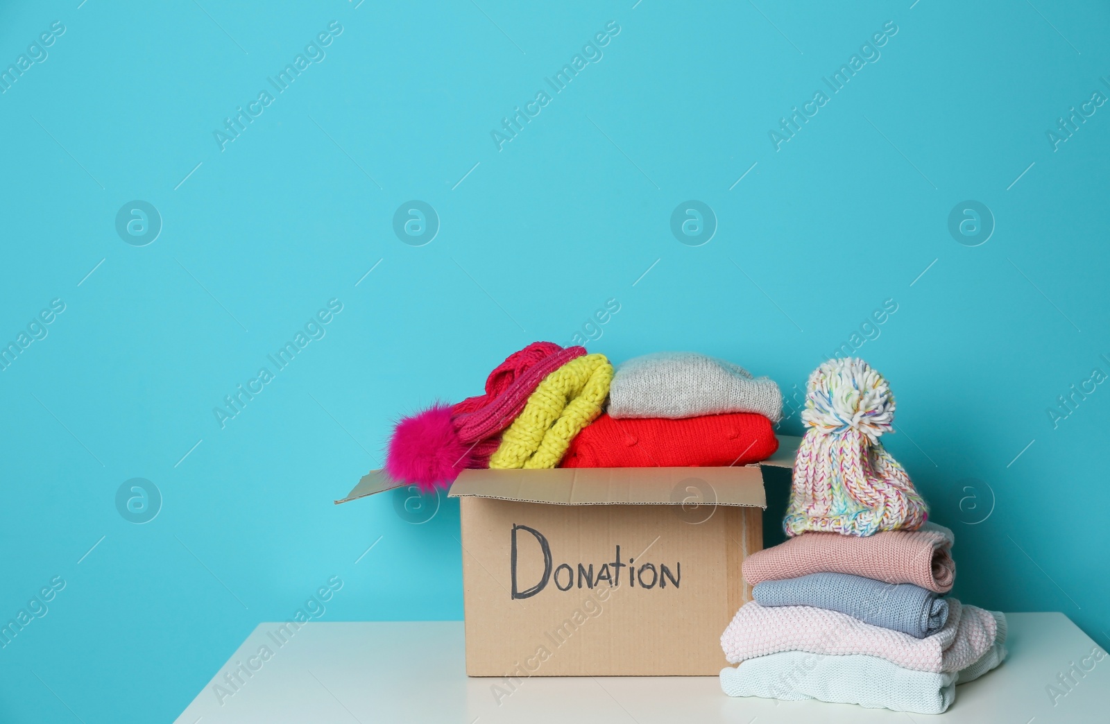 Photo of Donation box and knitted clothes on table against color background. Space for text