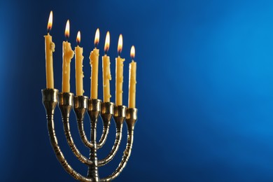 Photo of Hanukkah celebration. Menorah with burning candles on blue background, closeup and space for text