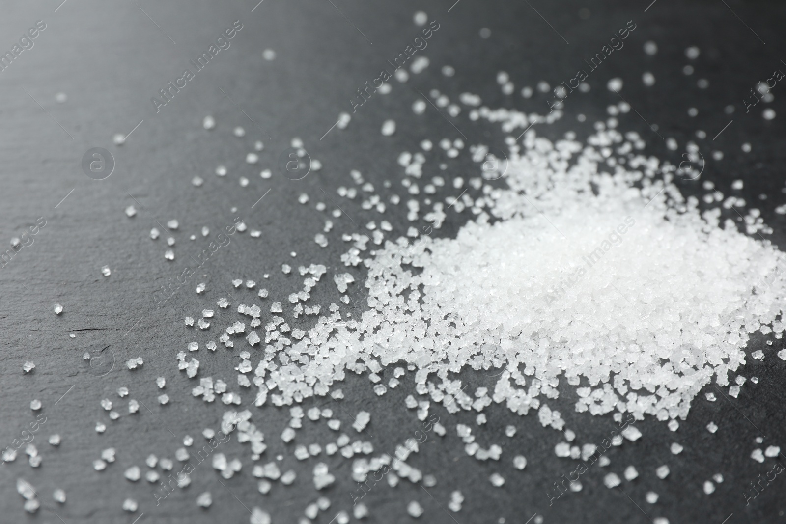 Photo of Heap of granulated sugar on black table, closeup. Space for text