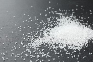 Heap of granulated sugar on black table, closeup. Space for text
