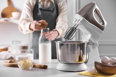 Photo of Woman adding sugar into bowl of stand mixer while making dough at table indoors, closeup