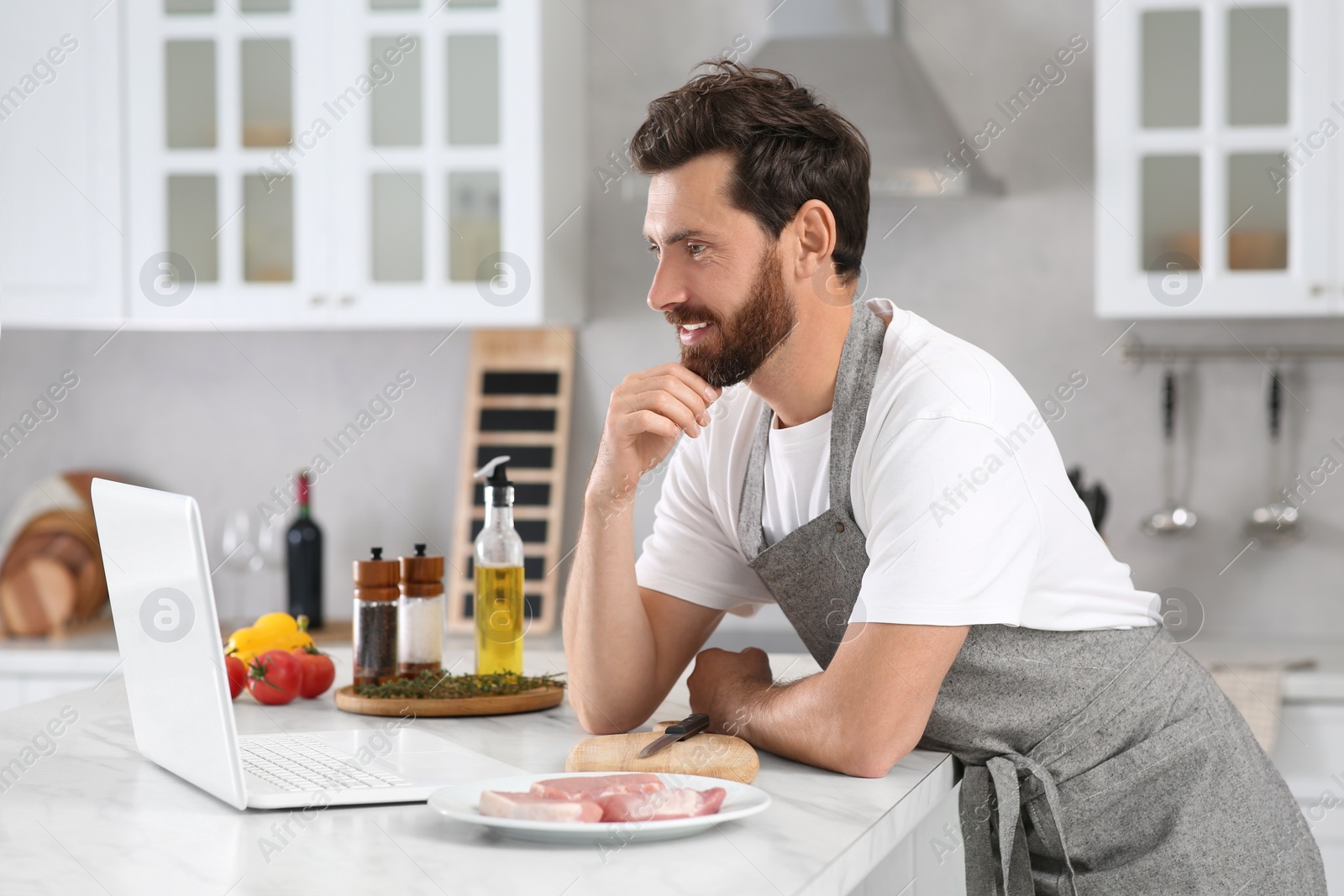 Photo of Man making dinner while watching online cooking course via laptop in kitchen