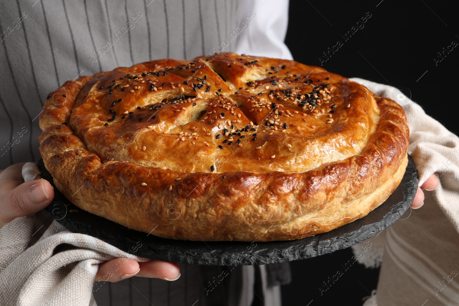 Photo of Woman holding tasty homemade pie on black background, closeup