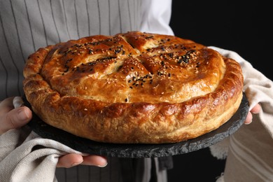 Photo of Woman holding tasty homemade pie on black background, closeup