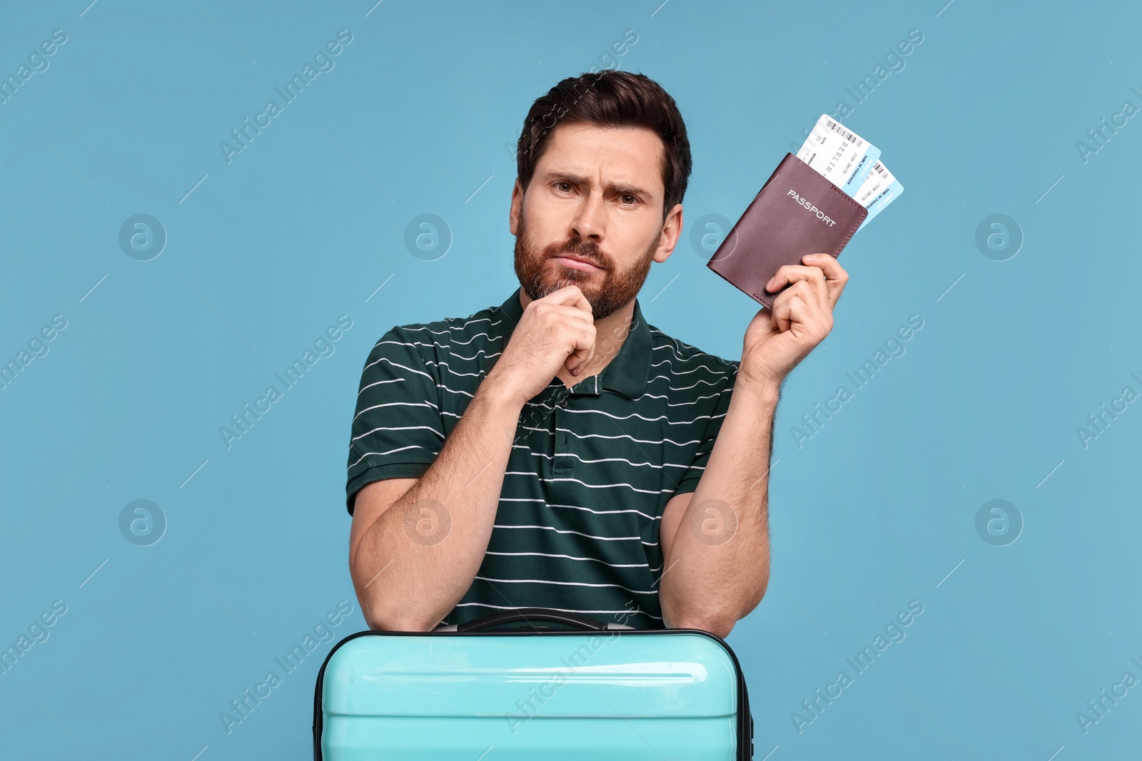 Photo of Thoughtful man with passport, suitcase and tickets on light blue background
