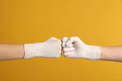 Photo of Doctors in medical gloves making fist bump on yellow background, closeup