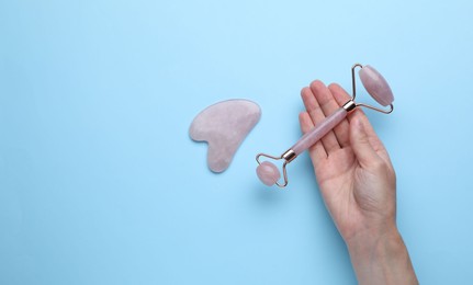 Photo of Woman holding gua sha tool and face roller on light blue background, top view. Space for text