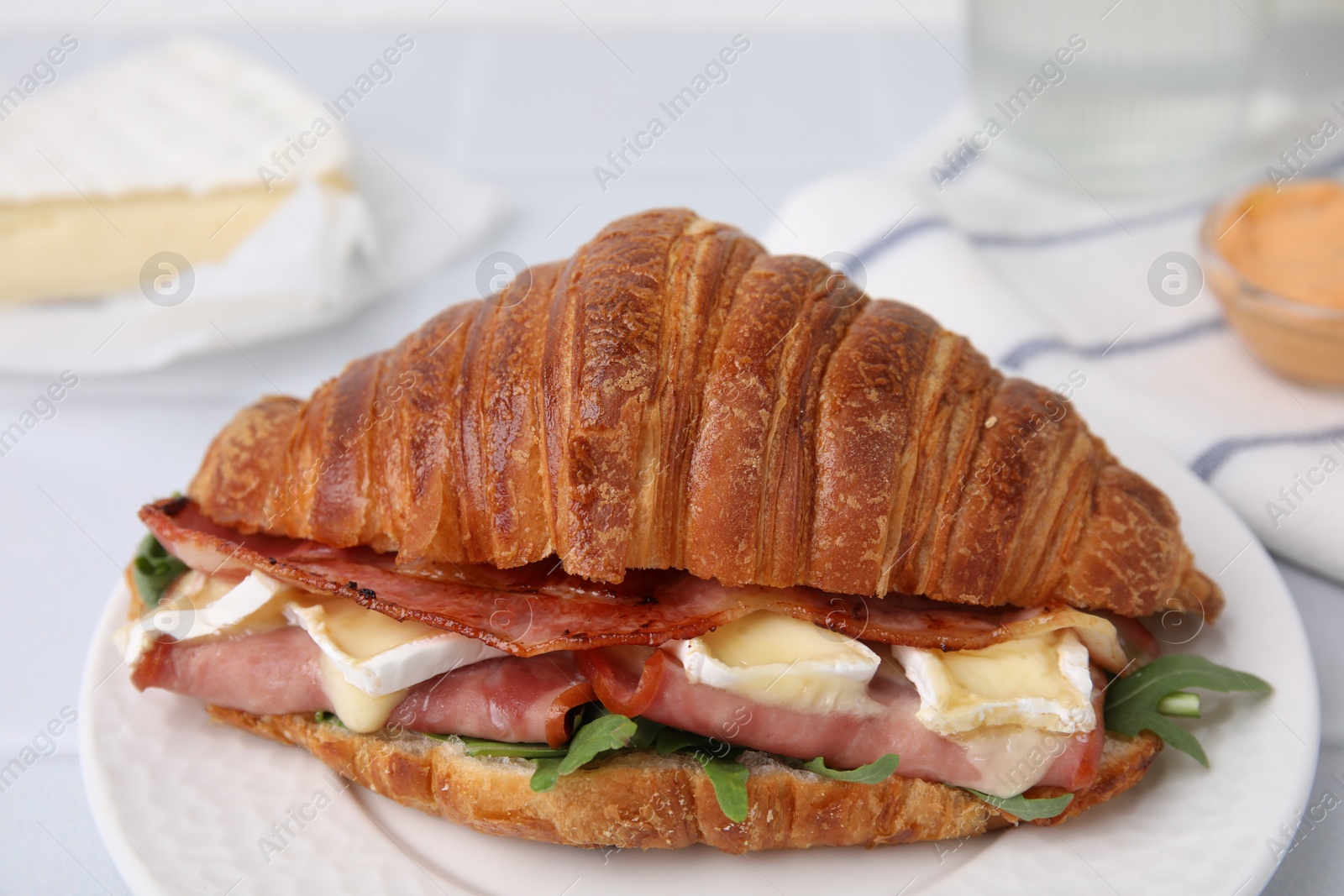 Photo of Tasty croissant with brie cheese, ham and bacon on white table, closeup