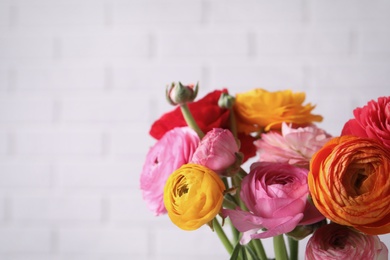 Photo of Beautiful fresh ranunculus flowers near white brick wall, closeup. Space for text