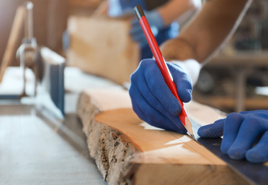 Professional carpenter making mark on wooden board in workshop, closeup