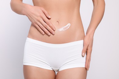 Photo of Woman applying body cream onto her belly against white background, closeup