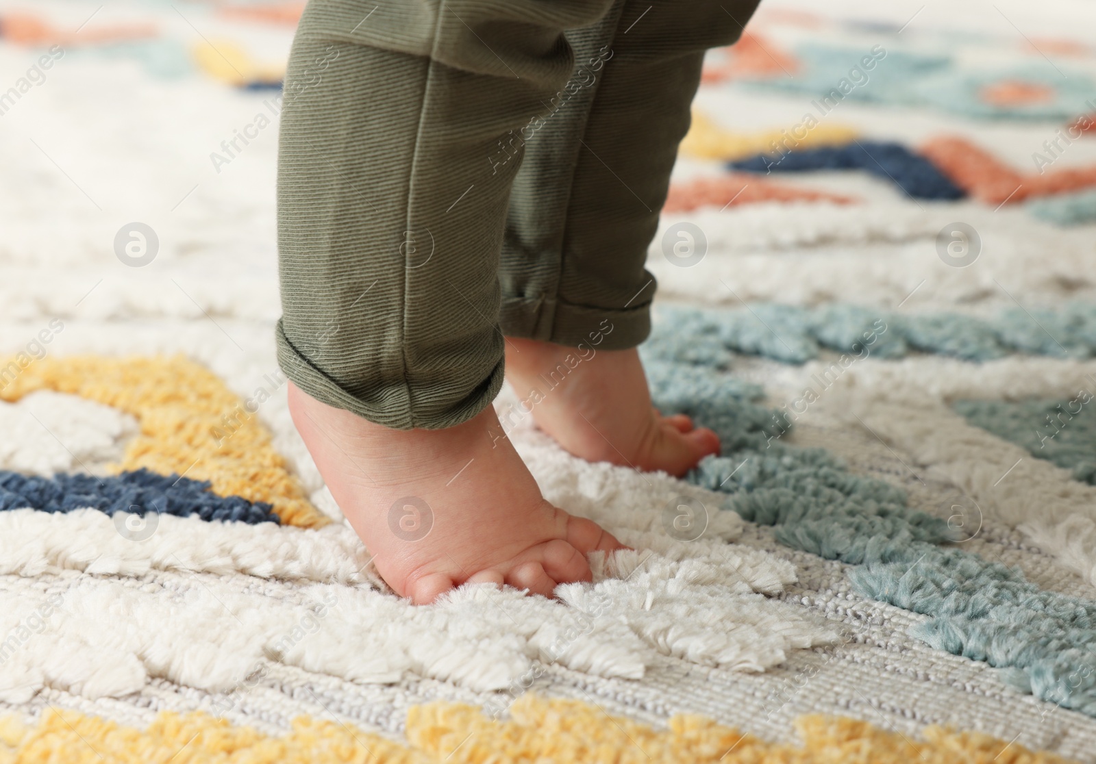 Photo of Baby standing on soft colorful carpet, closeup