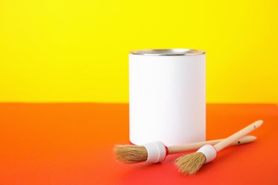 Photo of Blank can of paint with brushes on table against color background. Space for text