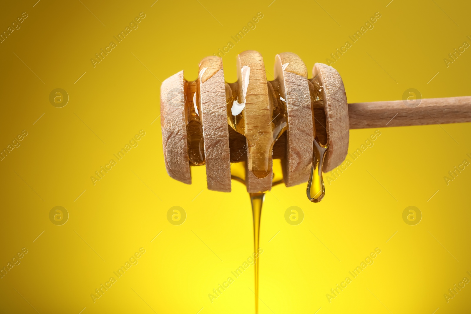 Photo of Delicious honey flowing down from dipper against yellow background, closeup