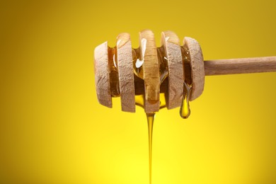 Delicious honey flowing down from dipper against yellow background, closeup