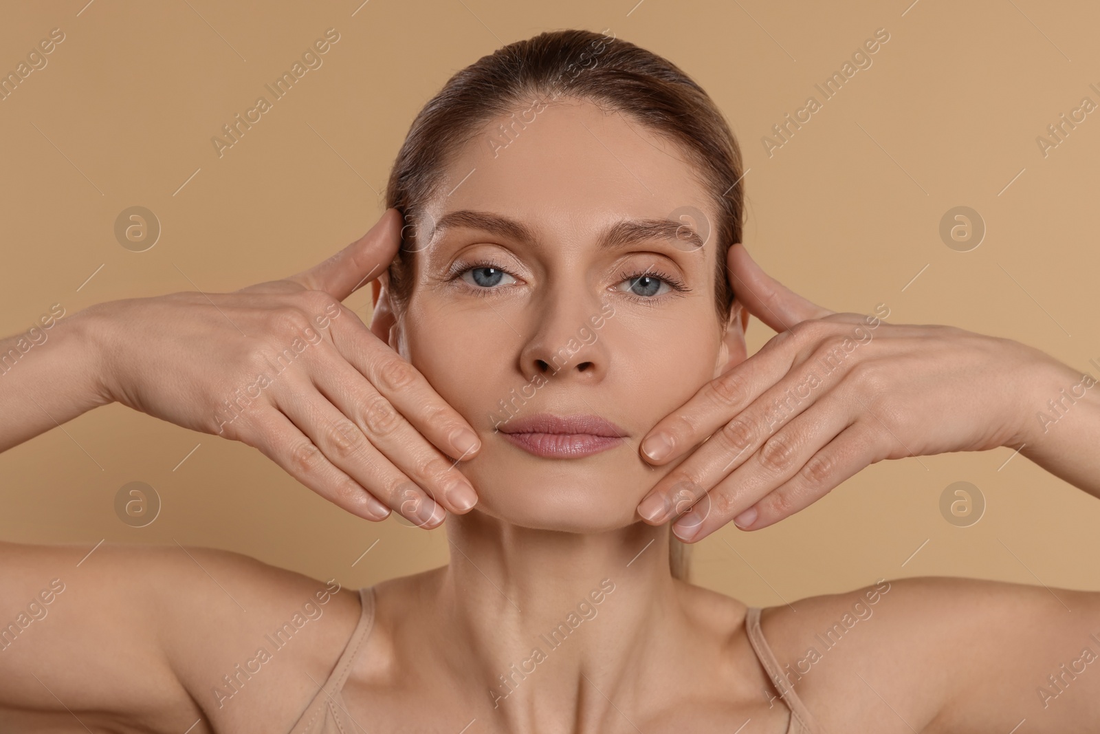 Photo of Woman massaging her face on beige background