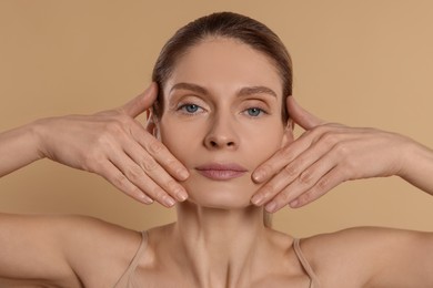 Woman massaging her face on beige background