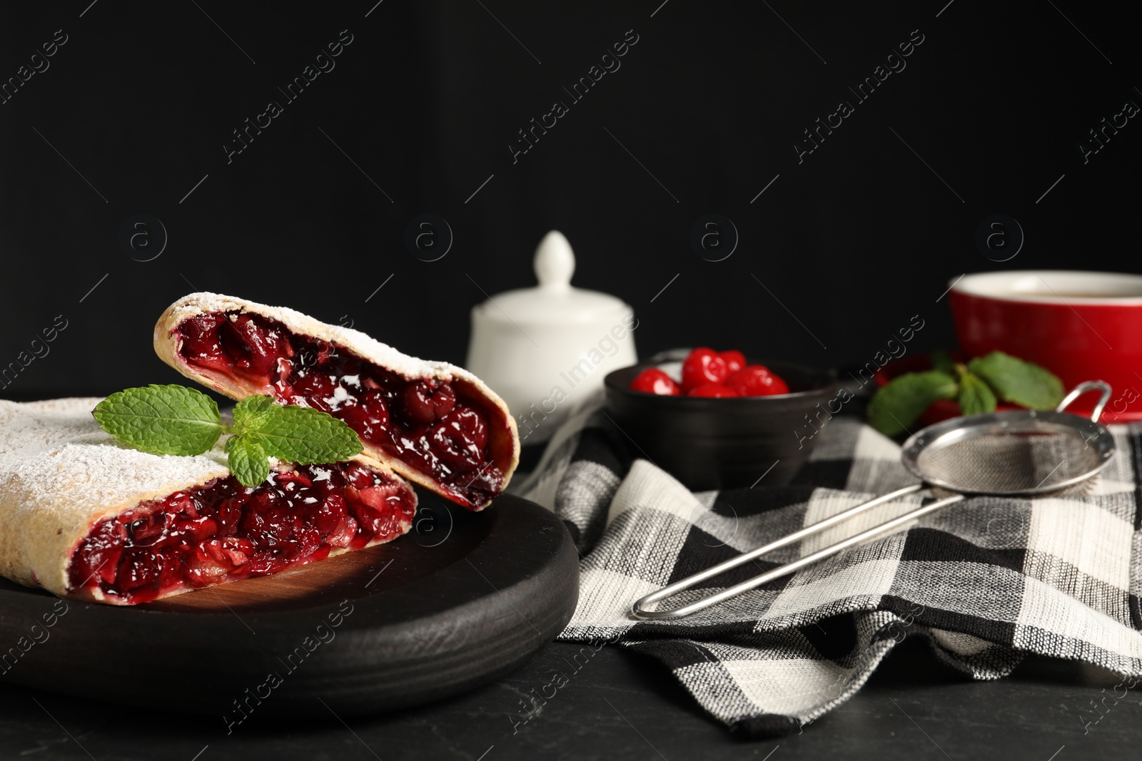 Photo of Delicious strudel with cherries, powdered sugar and mint on black table, closeup