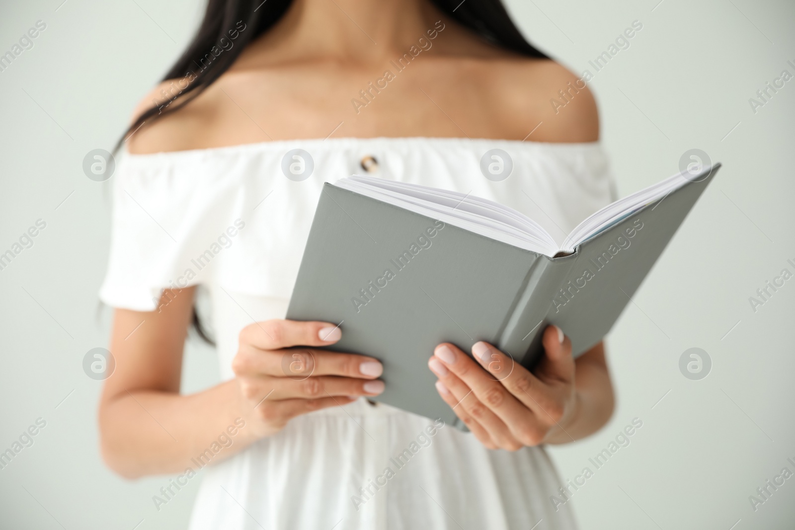 Photo of Young woman reading book on light grey background, closeup