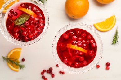 Photo of Tasty cranberry cocktail with rosemary and oranges in glasses on white table, flat lay