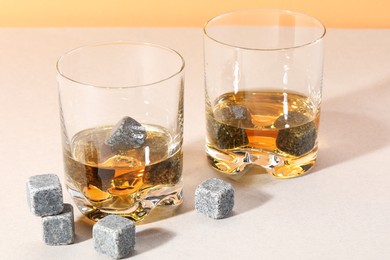 Whiskey stones and drink in glasses on light table, closeup