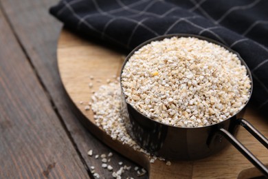 Photo of Raw barley groats in scoop on wooden table, closeup. Space for text